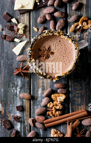 Vintage mug of hot chocolate, decor with nuts, caramel, spices. Ingredients above. Chopped dark and white chocolate, cocoa beans, anise over old woode Stock Photo