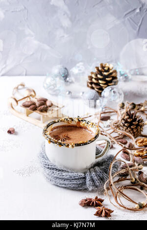 Vintage mug in wool scarf of hot chocolate, decor with nuts, caramel, spices. Ingredients and Christmas toys above over white texture background with Stock Photo