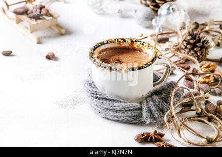 Vintage mug in wool scarf of hot chocolate, decor with nuts, caramel, spices. Ingredients and Christmas toys above over white texture background with Stock Photo