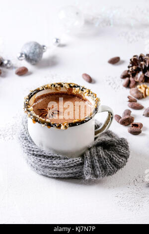 Vintage mug in wool scarf of hot chocolate, decor with nuts, caramel, spices. Ingredients and Christmas toys above over white texture background with Stock Photo