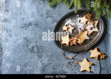 Homemade shortbread star shape sugar cookies different size with sugar powder on thread in vintage metal tray with fir branches over blue texture surf Stock Photo