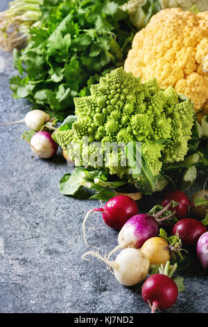 Variety of fresh raw organic colorful cauliflower, cabbage romanesco and radish with bundle of coriander over dark texture background. Close up with s Stock Photo