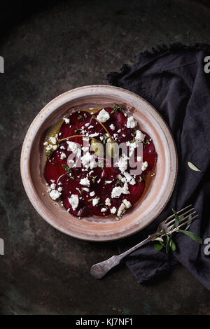 Vegetarian beetroot carpaccio salad with feta cheese, thyme, olive oil and capers in terracotta plate on textile napkin over old metal background. Top Stock Photo
