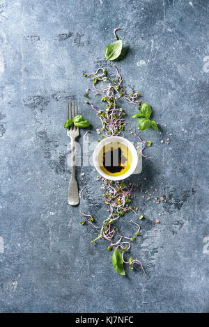 Young radish sprouts with pink himalayan salt and basil leaves with bowl of olive oil and balsamic vinegar over blue texture background. Top view with Stock Photo