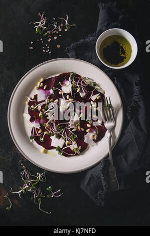Vegetarian beetroot carpaccio salads with olive oil, goat cheese, pine nuts and sprouts in white plate on textile napkin over dark rusty metal backgro Stock Photo