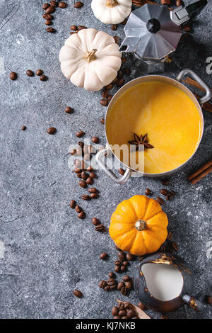 Ingredients for cook spicy pumpkin latte. Coffeepot, pumpkin milk in pan, jug of cream with spices, coffee beans and decorative pumpkins above over gr Stock Photo