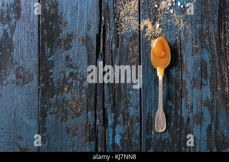 Homemade salted caramel sauce in vintage spoon with ingredients brown sugar and sea salt above. Over old dark blue wooden background. Top view with sp Stock Photo