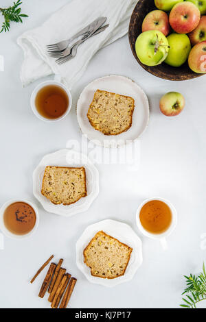 Cinnamon apple bread slices served on three white plates photographed from top view. Three cups of tea and apples in a wooden bowl accompany. Stock Photo