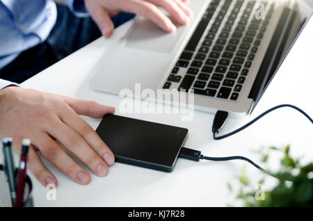 External backup disk hard drive connected to laptop. Man with notebook making safety personal data copy. Stock Photo