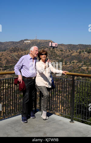 Senior couple holding selfie stick taking cell phone photo in front of Hollywood sign Griffith Park Observatory Los Angeles, California  KATHY DEWITT Stock Photo