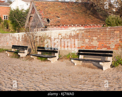 three empty benches outside on beach near wall ; west mersea, essex, england, uk Stock Photo
