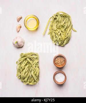 green pasta with spinach and cherry tomatoes, laid out on a white background with the wooden rustic spices, oil and garlic Stock Photo