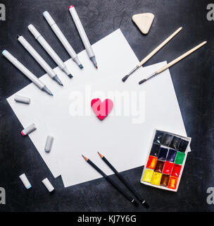 concept of a workplace of the artist, of paper lie on a black table, laid out around a variety of water colors and brushes, colored pencils and marker Stock Photo