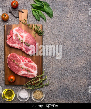 Ingredients for cooking Two fresh raw pork steaks with seasonings and herbs, cherry tomatoes and butter, lined on a cutting board top view border Stock Photo