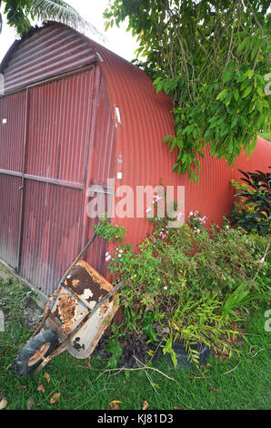 Old wheelbarrow leaning against metal corrugated shed on the island of Mare in the Loyalty Islands New Caledonia Stock Photo