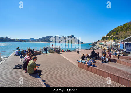 San Sebastian (Donostia), Spain - March 16. People enjoying a sunbathing in footbridge of leisure harbour of San Sebastian with Santa Clara island and Stock Photo