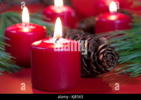 Closeup of burning red Christmas candles with pine needles and cones Stock Photo