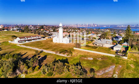 White historic Macquarie lighthouse on elevated South Head headland overlooking Watsons bay eastern suburb in Sydney with city CBD and harbour in back Stock Photo