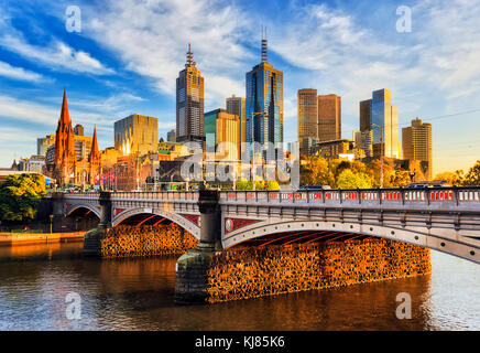 Warm morning light on high-rise towers in Melbourne CBD above Princes bridge across Yarra river.