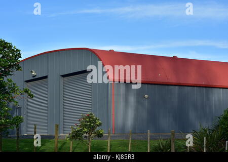 Large barn made from corrugated sheet metal painted gray on walls and red on roof. Stock Photo