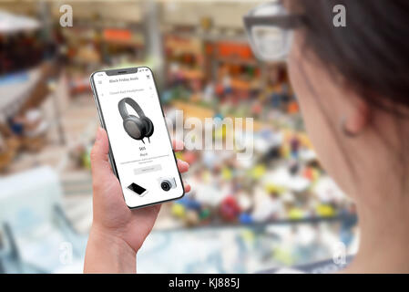 Shopping with mobile phone. Online discount on Black friday sale. Woman holding modern mobile phone. Shopping mall in background. Stock Photo