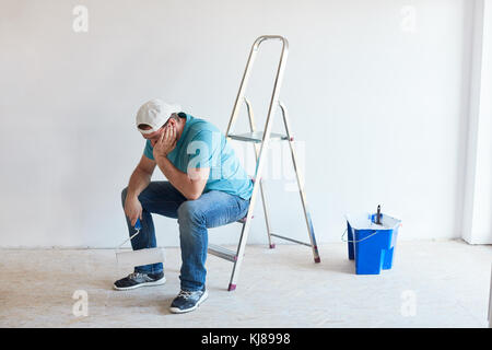 Tired man sitting on ladder holding a roller in front of him Stock Photo