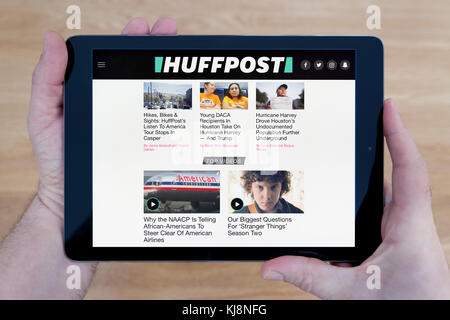 A man looks at the Huffington Post website on his iPad tablet device, shot against a wooden table top background (Editorial use only) Stock Photo