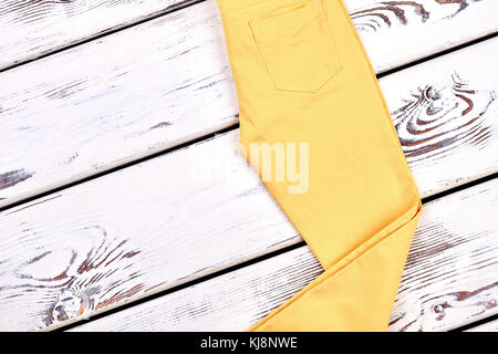 Girls new yellow trousers. Young lady yellow color pockets pants folded on  white wooden background. Woman fashion clothes store Stock Photo - Alamy