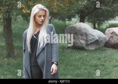 Portrait of young blondhair elegantly dressed woman in a coat with smart bracelet standing outdoor. Stock Photo