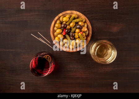 An overhead photo of a tapas mix of olives, mini gherkins, and other pickles, shot from above on a rustic texture with glasses of wine, toothpicks, an Stock Photo