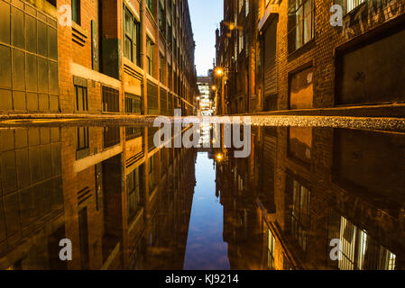A low point of view over a puddle looking down Back China Lane from Dale Street, central Manchester. Stock Photo