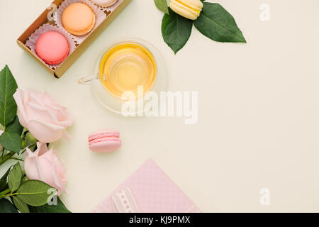 Colorful macaroons and rose flowers with tea on light green. Sweet macarons in gift box. Top view Stock Photo