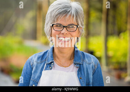 Beautiful mature woman working in a greenhouse, looking at camera and smiling Stock Photo