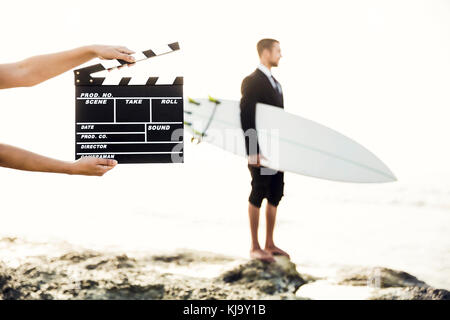Businessman in front of a clapboard holding is surfboard. Concept about a man starting a new life. Stock Photo