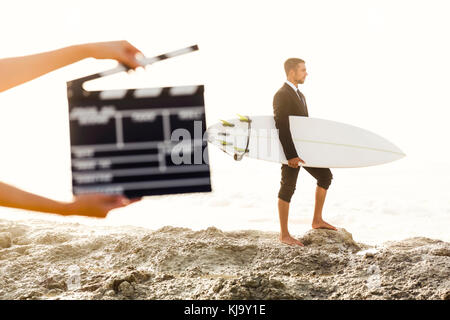 Businessman in front of a clapboard holding is surfboard. Concept about a man starting a new life. Stock Photo