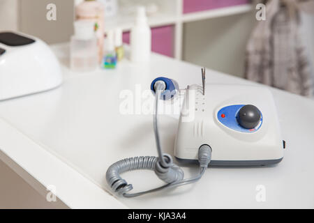 Drill for manicure on a light table with blurry cosmetics in the background. Stock Photo
