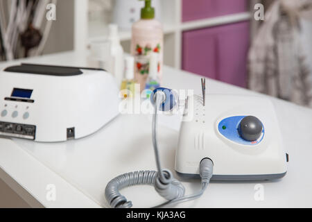 Drill for manicure on a light table with blurry cosmetics in the background. Stock Photo