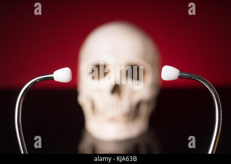 Stethoscope i focus and blurry skull isolated on black red background Stock Photo