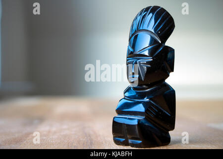 An aztec obsidian ancient statuette on wooden table in sunlight. Stock Photo