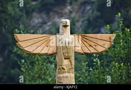 Wooden carved eagle on top of huge totem pole Stock Photo