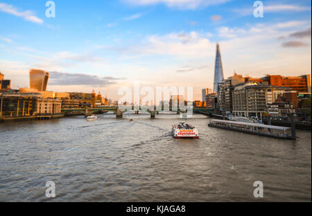 View from Millennium footbridge towards the Shard and Tower Bridge with a City Cruises boat passing on the River Thames. With Tilt Shift effect. Stock Photo