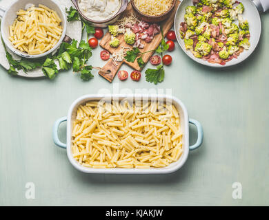 Cooking preparation of pasta casserole with romanesco cabbage and ham in creamy sauce ready for bake, on kitchen table background with ingredients Stock Photo
