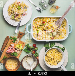 Pasta casserole with romanesco cabbage and ham in creamy sauce,  served in plate with cutlery on kitchen table with ingredients, top view. Stock Photo