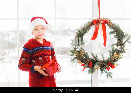 Portrait of cute little child in holiday christmas interior. Happy smiling kid posing for photo standing near big window with snowy city landscape see Stock Photo