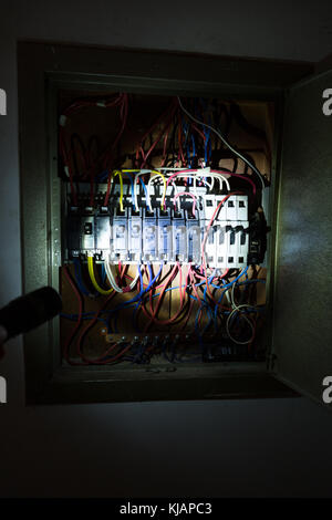 LED flashlight torch lamp illuminating part of old circuit breaker  switch, cables and wires on panel is seen inside house, Asuncion, Paraguay Stock Photo