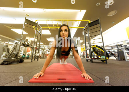 A beautiful young girl working on her arm muscles by performing push ups in the Gym. Stock Photo