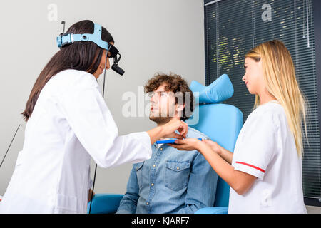 A female Ear-Nose-Throat aka ENT specialist doctor diagnosing a young male patient. Stock Photo