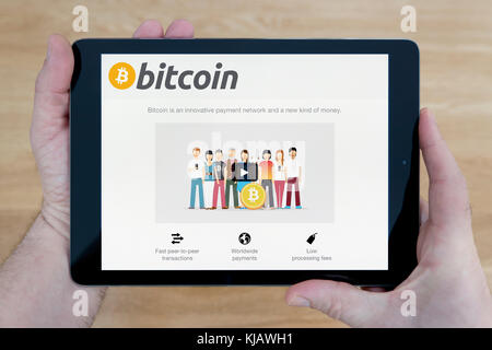 A man looks at the Bitcoin website on his iPad tablet device, shot against a wooden table top background (Editorial use only) Stock Photo