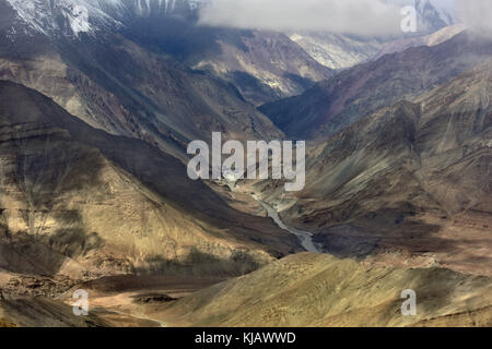 Mountain valley: a ravine from high mountains, the river is muddy gray on the bottom, the hillsides are illuminated by the sun and covered by clouds,  Stock Photo