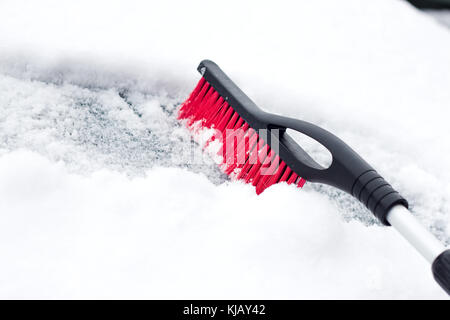 Transportation, winter, weather, people and vehicle concept - man cleaning snow from car with brush . Stock Photo